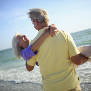 Senior man carrying his wife on the beach