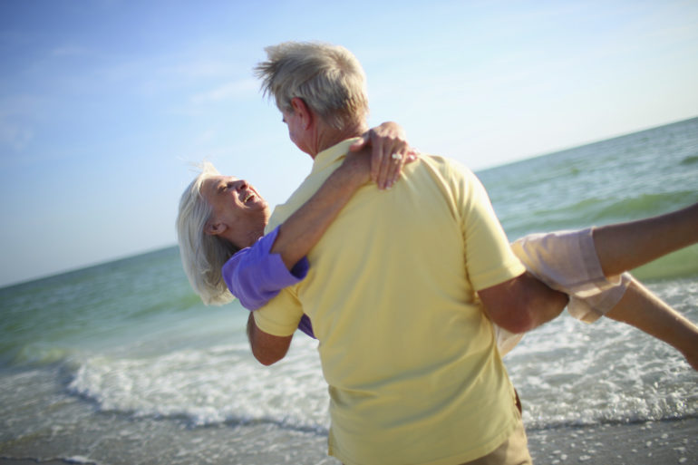Senior man carrying his wife on the beach