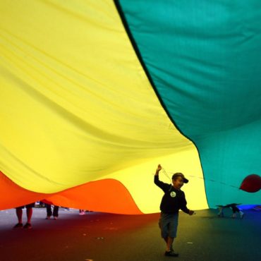 A child holds a balloon under a Pride flag held by participants marching during Seattle's annual Gay Pride Parade on Sunday, June 24, 2012. (AP Photo/seattlepi.com, Joshua Trujillo)