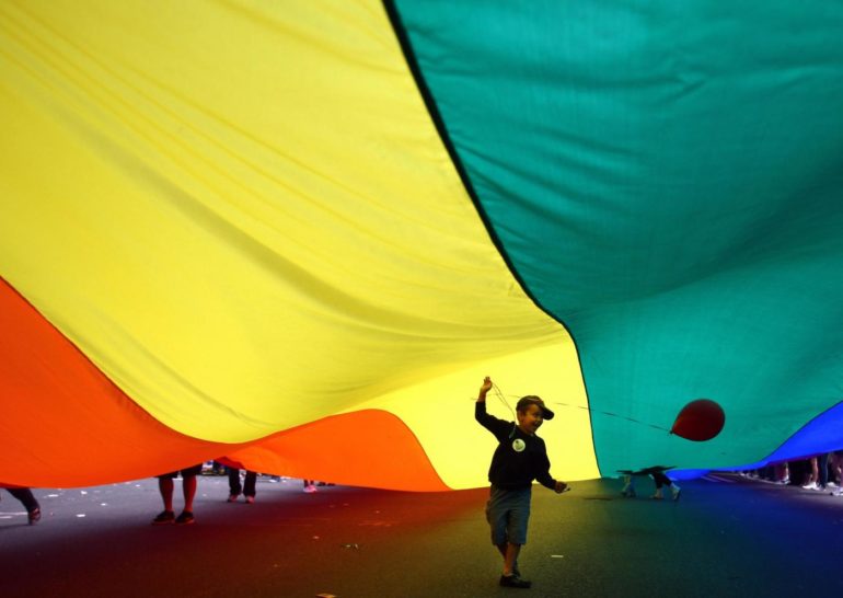 A child holds a balloon under a Pride flag held by participants marching during Seattle's annual Gay Pride Parade on Sunday, June 24, 2012. (AP Photo/seattlepi.com, Joshua Trujillo)
